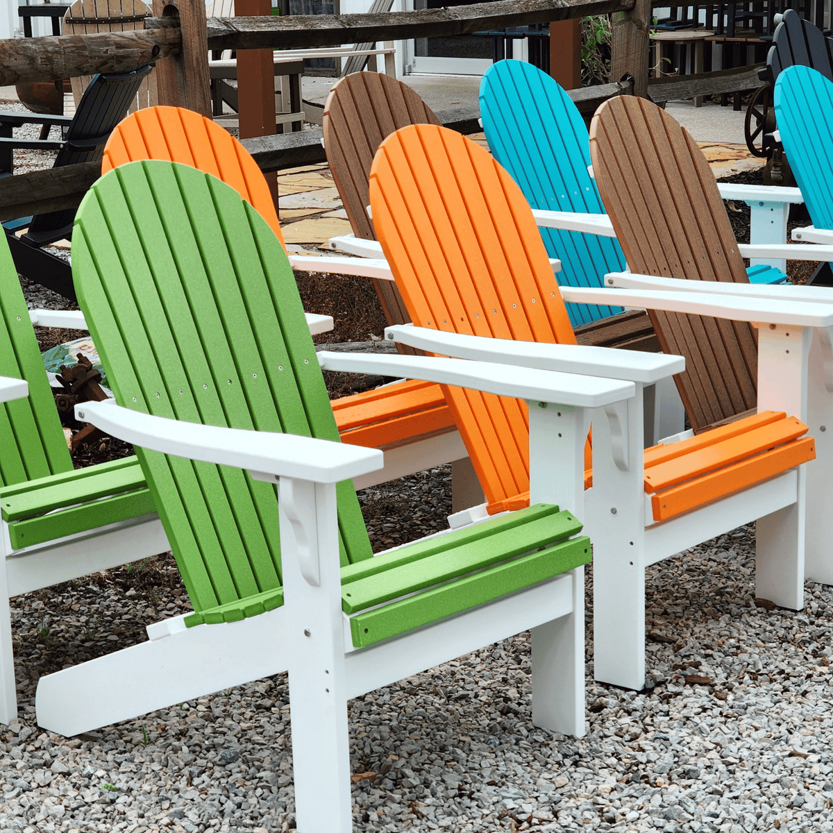 Colorful Adirondack chairs on a gravel surface with wooden tables in the background.