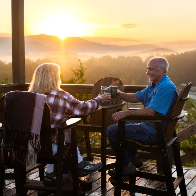Two people sitting at a wooden table on a deck, enjoying a sunset view.