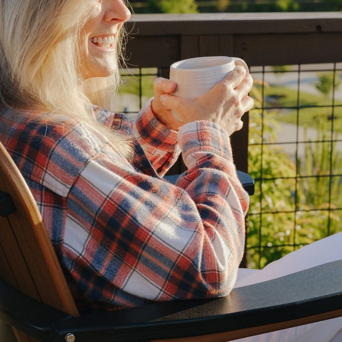 Person wearing a plaid shirt holding a cup outdoors