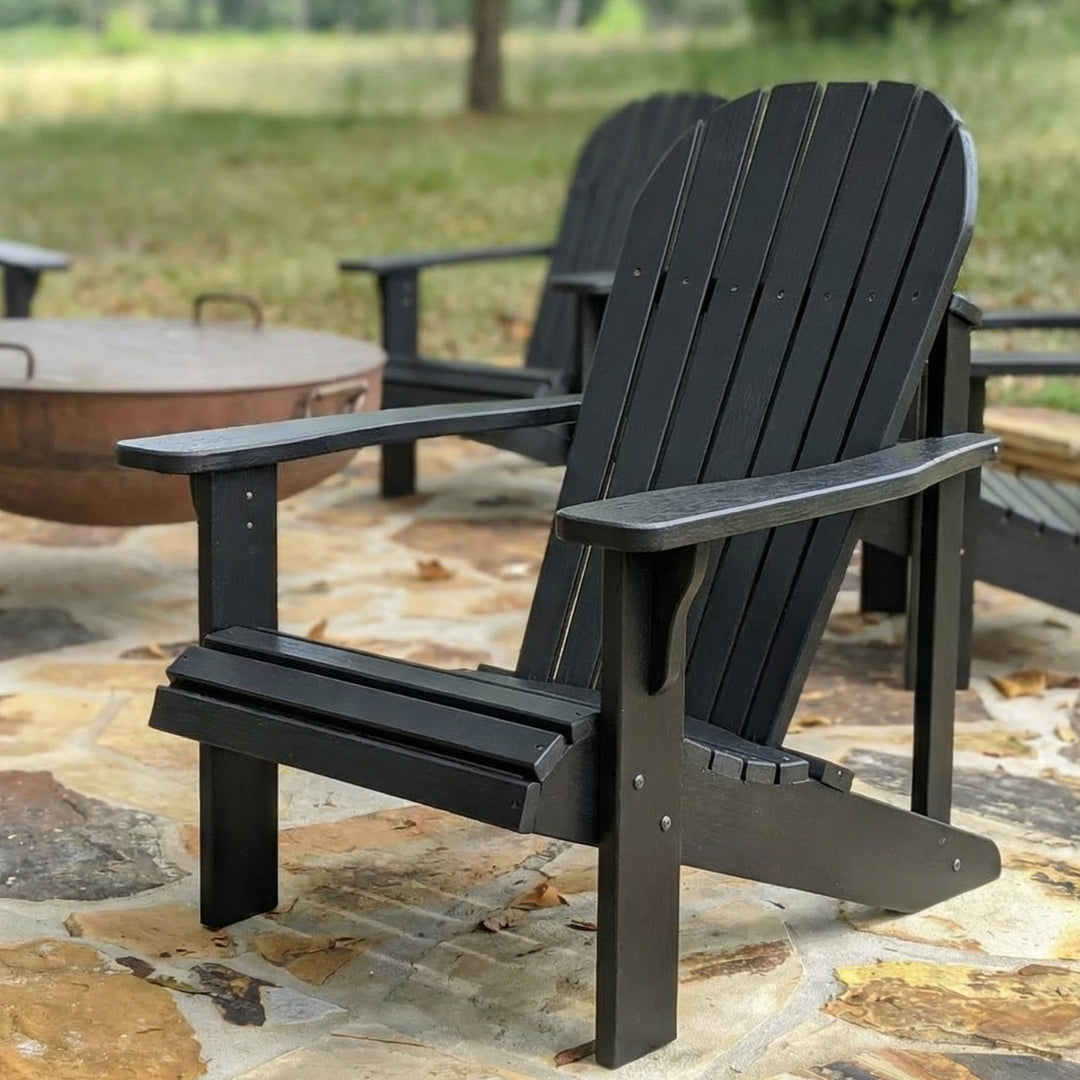 Black Adirondack chair on a stone patio with a fire pit in the background