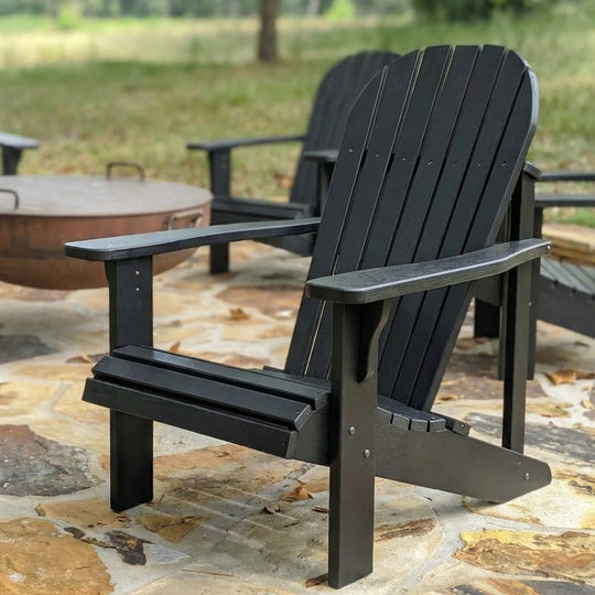 Black Adirondack chair on a stone patio with a fire pit in the background