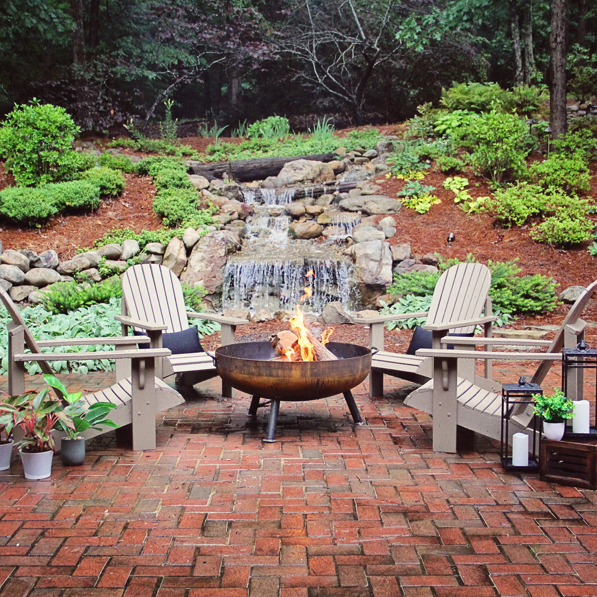 Outdoor patio with fire pit, chairs, and a small waterfall in a garden setting.