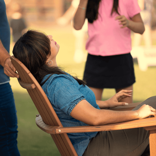 Woman sitting in a wooden chair outdoors with people in the background