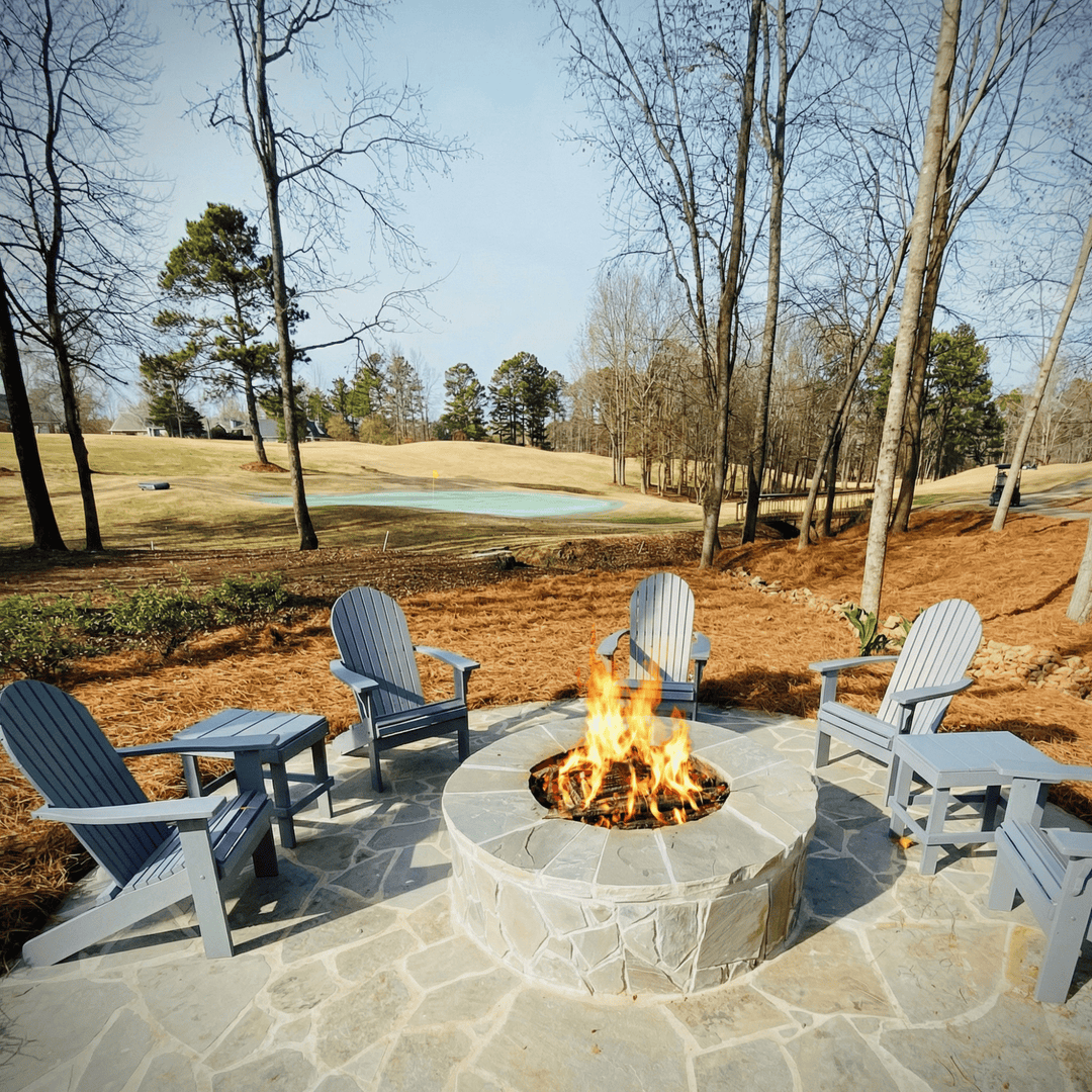 Fire pit with Adirondack chairs in a park-like setting with trees and grass.
