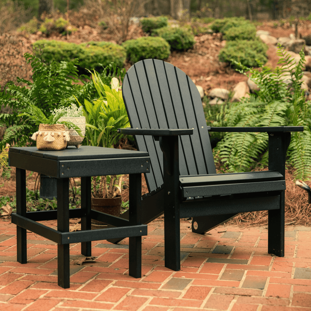 Black Adirondack chair and table set on a brick patio with greenery in the background