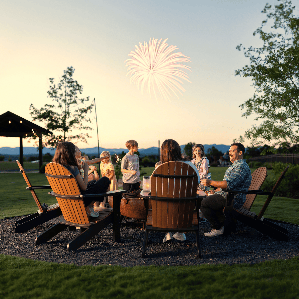 People sitting around a fire pit with fireworks in the background