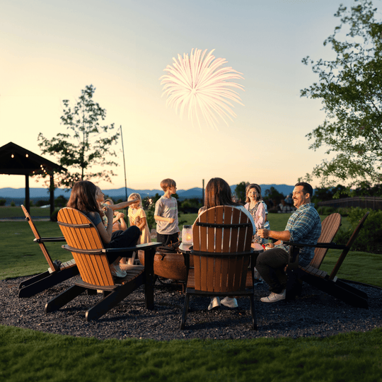 People sitting around a fire pit with fireworks in the background